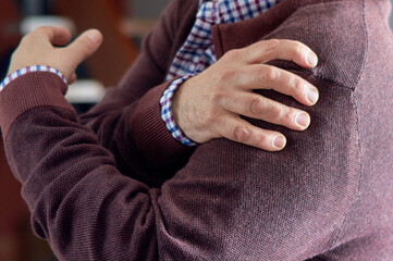 An man puts his hand on his shoulder because he has pain due to osteoarthritis, arthritis, or rheumatism.