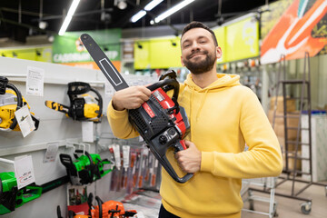 Fototapeta premium happy buyer in the store with a petrol saw in his hands happy looking at the camera