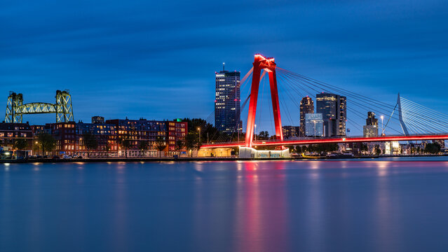 A stunning view of Rotterdam's city skyline, featuring the Willemsbridge and the Hef bridge illuminated by the twilight sky