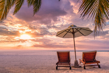 Beautiful tropical sunset scenery, two sun beds, loungers, umbrella under palm tree. White sand, sea view with horizon, colorful twilight sky, calmness and relaxation. Inspirational beach resort hotel