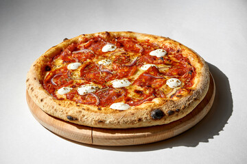 Crispy pizza with salami, onions and cream cheese on a gray background.