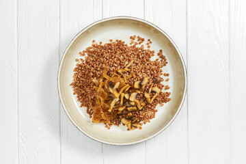 Buckwheat porridge with mushroom in a plate on a white wooden background