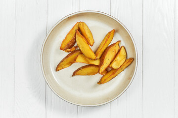 Baked potato wedges in a plate on a white wooden background.