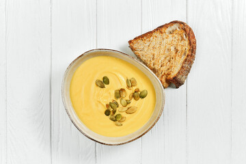 Pumpkin cream soup with seeds in a plate on a white wooden background.