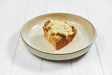 Toast with baked cheese and chicken in a plate on a white wooden background.