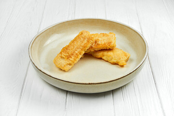 Fried fish in batter in a plate on a white wooden background.
