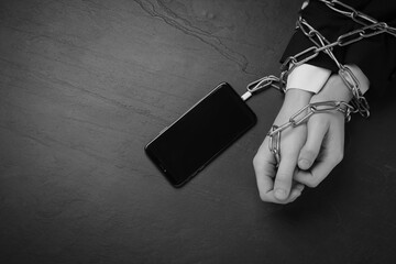 Top view of internet addicted woman chained to smartphone at dark table, space for text. Black and...