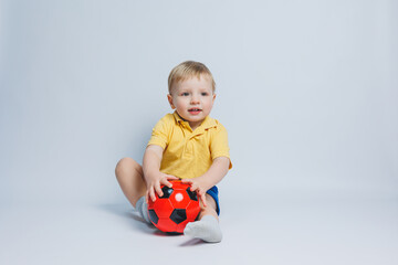 Boy 3-4 years old football fan in a yellow T-shirt with a ball in his hands, holding a soccer ball in his hands, isolated on a white background. The concept of sports family recreation