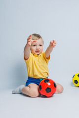 Little cute kid baby boy 3-4 years old, football fan in red t-shirt holding in hand soccer ball isolated on yellow background. Kids sport family leisure lifestyle concept. Copy space advertisement