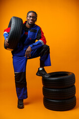 African american car service worker with car tyre against yellow background © fotofabrika