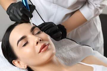 Young woman undergoing procedure of permanent eyebrow makeup in salon, closeup