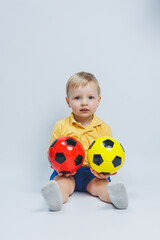 Little european boy, fan or player in yellow and blue uniform with a soccer ball, supports the soccer team on a white background. Football sport game, lifestyle concept. Isolated on white background