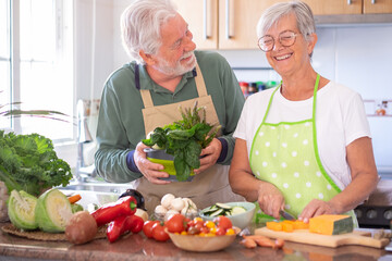 Attractive senior couple preparing vegetables together in the home kitchen laughing amused....