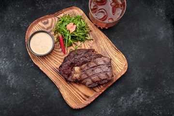 Grilled steak with sauce, herbs and a glass of whiskey, on a wooden board