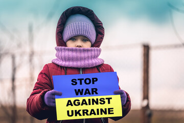 A little refugee girl with a sad look on her face and a Ukrainian flag that says stop war against...