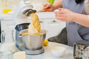 A women cook cleans the whisk of the mixer after kneading the dough.