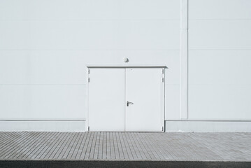 Exterior of industrial building, closed white double door. Emergency exit or entrance, frontal view...