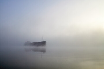 Misty morning on the river. Big cargo ship fading in the mist. Fog covering river. Danube river in the misty morning