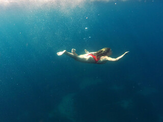 Young woman swims underwater in blue sea