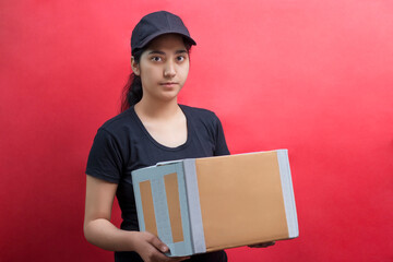 Portrait Of Young Delivery Woman Holding Cardboard Box Against Color Background