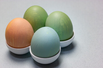 Four Easter Eggs standing in egg tray on a table on a light blue-grey background. A group of green, blue, brown colored hand-painted eggs. Traditional Easter food concept. Soft natural pastel colors.