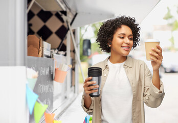 sustainability and people concept - portrait of happy smiling woman with coffee cup and tumbler for hot drinks over food truck background