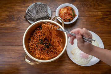 Hand using chopsticks to pick up  Ramyeon noodle in a traditional korean noodle pot, Spicy Korean Ramyeon instant noodle a traditional dish.