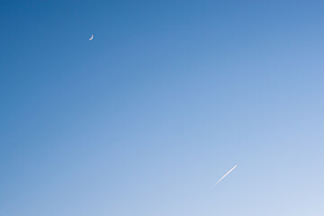 There is an airplane and the moon in the sky.