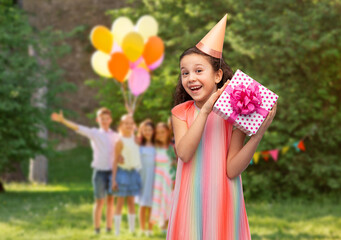 birthday, childhood and people concept - portrait of smiling little girl in dress and party hat with gift box over group of children at summer park background