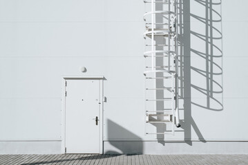 Building exterior, sandwich panel wall, white door and steel staircase. Frontal view of an emergency entrance or fire exit to an industrial building, outdoors