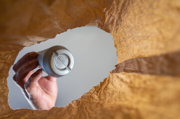 A hand retrieves a gray plastic bottle in a paper bag. A mature man's hand holds a sweet ice cream topping over an open brown bag. Shot from the bottom up. Close up. Selective focus.