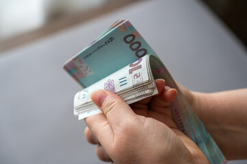 A grown woman counts money indoors. Her hands are holding a bundle of Ukrainian hryvnias. Banknotes in denominations of 1000 hryvnia. Selective focus