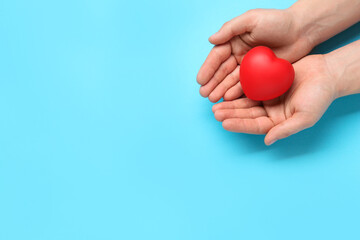 Man holding red decorative heart on light blue background, top view and space for text. Cardiology concept