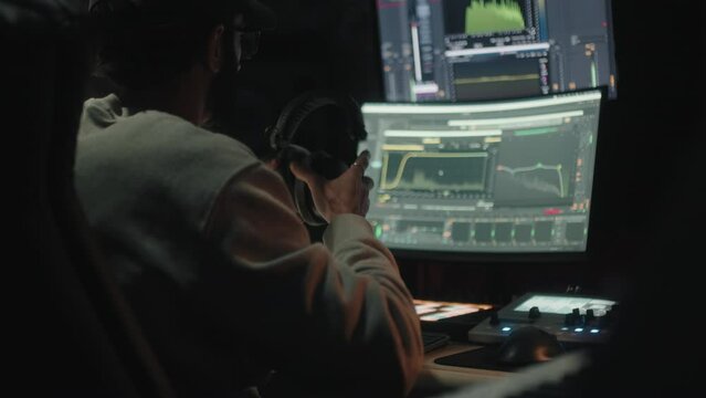 Sound engineer seen seated from behind uses the computer to mix audio music