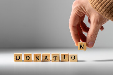 charity and financial help concept - close up of hand making donation word with wooden toy blocks