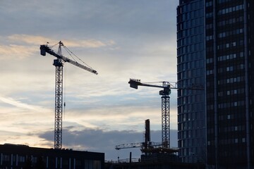 Budowa apartamentowca z dźwigiem budowlanym podczas budowy na tle błękitnego wieczornego nieba z chmurami - obrazy, fototapety, plakaty