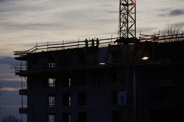 Budowa apartamentowca z dźwigiem budowlanym podczas budowy na tle błękitnego wieczornego nieba z chmurami - obrazy, fototapety, plakaty