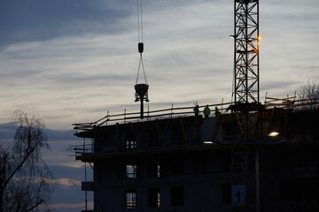 Budowa apartamentowca z dźwigiem budowlanym podczas budowy na tle błękitnego wieczornego nieba z...