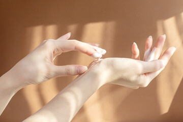 Beautiful female hands close-up apply moisturizer to delicate skin on brown background in rays of...