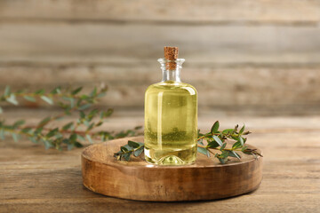 Bottle of eucalyptus essential oil and plant branches on wooden table