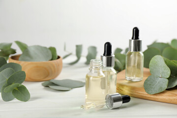 Bottles of eucalyptus essential oil and plant branches on white marble table