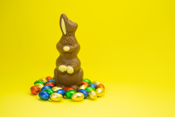 Easter. A chocolate bunny on a yellow background and colorful eggs and sweets are scattered around. Holiday concept, promotions, sale, gifts, discounts mockup. High quality photo