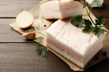 Tasty salt pork with herbs, onion and garlic on wooden table, closeup