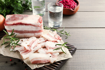 Tasty salt pork with rosemary and pepper on wooden table, space for text