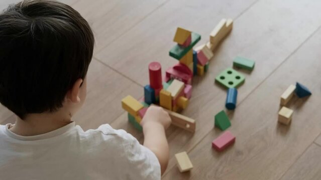 Back view little boy building tower of block toys sitting on floor. Having fun and learning creativity. Smart kid concept.