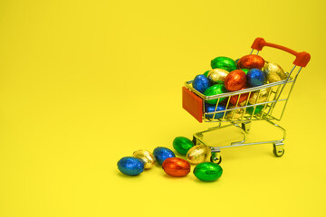 shopping trolley filled with multi-colored chocolates on a yellow background. The concept of shopping, business, discounts, advertising High quality photo