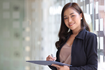 Portrait of a smiling beautiful Asian businessman holding a document writing and standing in the office. Looking at camera.