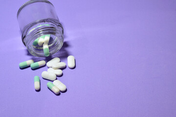 Close up, medicines, in pills on the light mauve background and in a small glass container. Copy space.