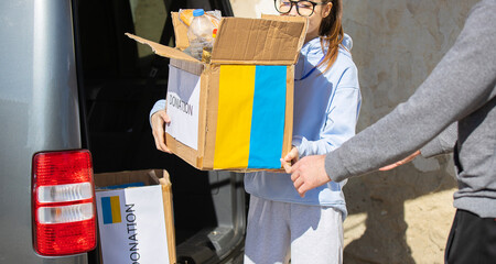 Young woman giving the cardboard box with food to a volunteer man for distribiyion among the ukranian refugees.