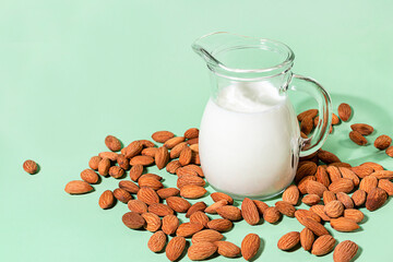 Almond milk in a glass jug and almond kernels on a green background, non-milk, natural organic product